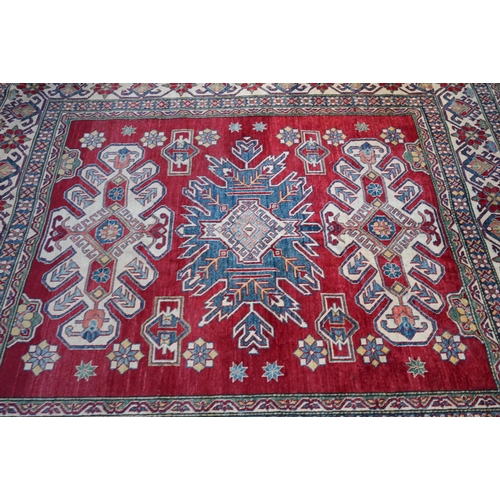 1228 - A contemporary Kazak carpet with pale red ground and stylized floral design within camel ground bord... 