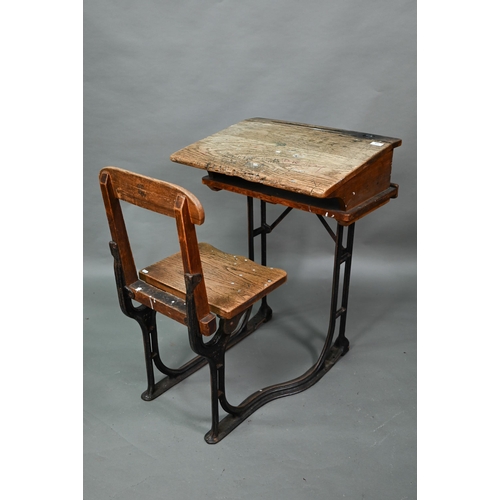 893 - A Victorian cast iron and oak student/school desk, the slope top carved with multiple graffiti, rais... 