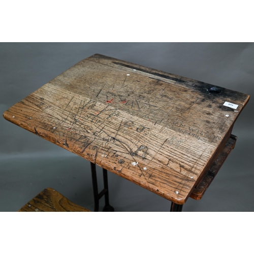 894 - A Victorian cast iron and oak student/school desk, the slope top carved with multiple graffiti, rais... 