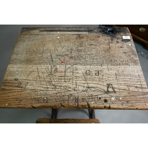 894 - A Victorian cast iron and oak student/school desk, the slope top carved with multiple graffiti, rais... 