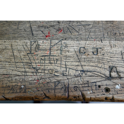 894 - A Victorian cast iron and oak student/school desk, the slope top carved with multiple graffiti, rais... 