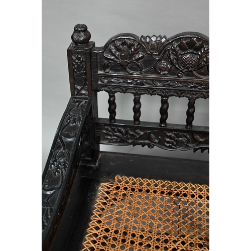 934 - A profusely carved and moulded colonial ebonised hardwood sofa bench, with cane panelled seat (with ... 