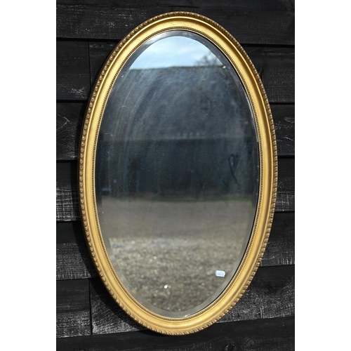 126 - An Edwardian bevelled oval wall mirror in decorative moulded gilt frame, 84 x 54 cm