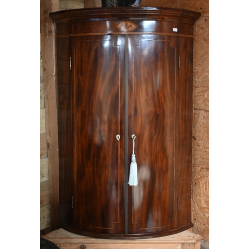 102 - A Georgian inlaid mahogany bowfront corner cupboard, brass fittings