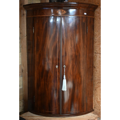 102 - A Georgian inlaid mahogany bowfront corner cupboard, brass fittings