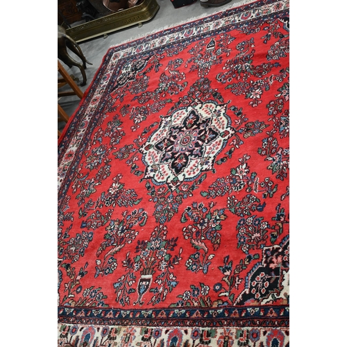 188 - An Indo-Persian Sarouk carpet, the traditional floral design on red ground with ivory palmette borde... 