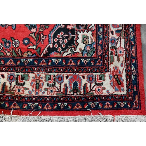 188 - An Indo-Persian Sarouk carpet, the traditional floral design on red ground with ivory palmette borde... 