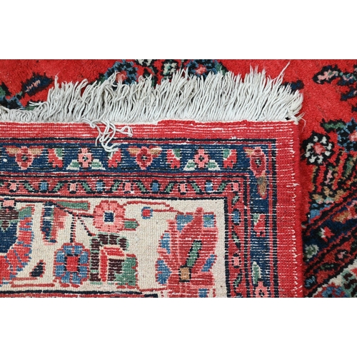 188 - An Indo-Persian Sarouk carpet, the traditional floral design on red ground with ivory palmette borde... 