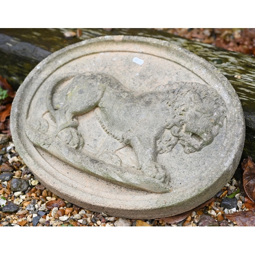 110A - A weathered reconstituted stone oval wall plaque cast in relief with a prowling lion, 48 cm wide