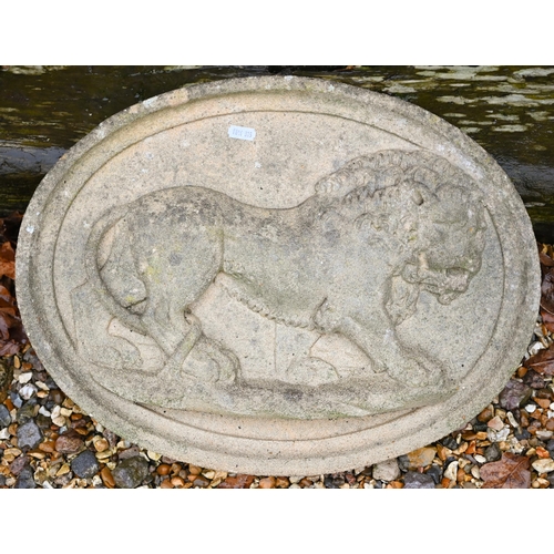 110A - A weathered reconstituted stone oval wall plaque cast in relief with a prowling lion, 48 cm wide