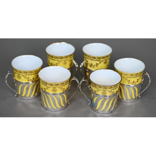17 - An Edwardian set of six Spode yellow and gilt coffee cans, in pierced silver holders with scroll han... 
