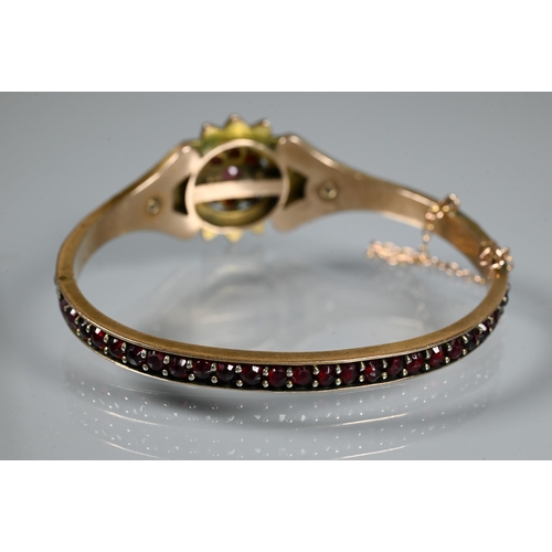 243 - A Victorian garnet-set bangle, the oval half-hinged yellow metal bangle with central flower motif, c... 