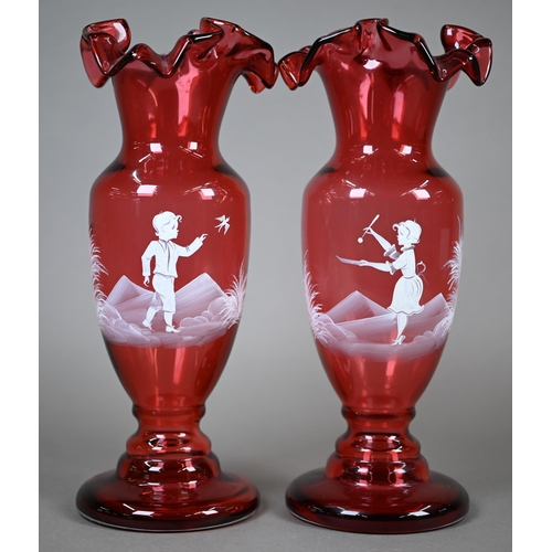 556 - A pair of cranberry glass vases with crenellated rims and waisted stems, painted with children playi... 