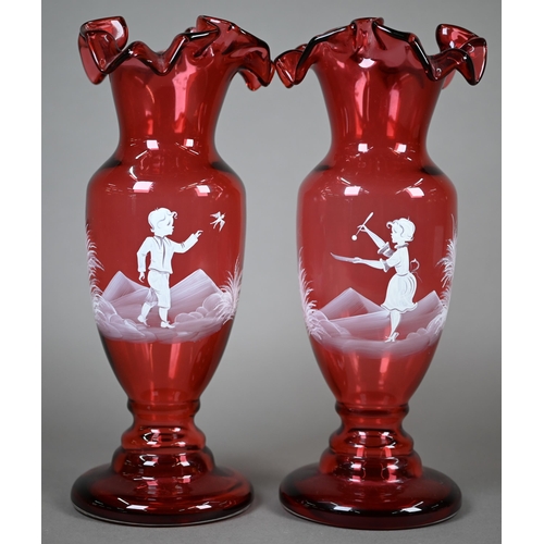 556 - A pair of cranberry glass vases with crenellated rims and waisted stems, painted with children playi... 