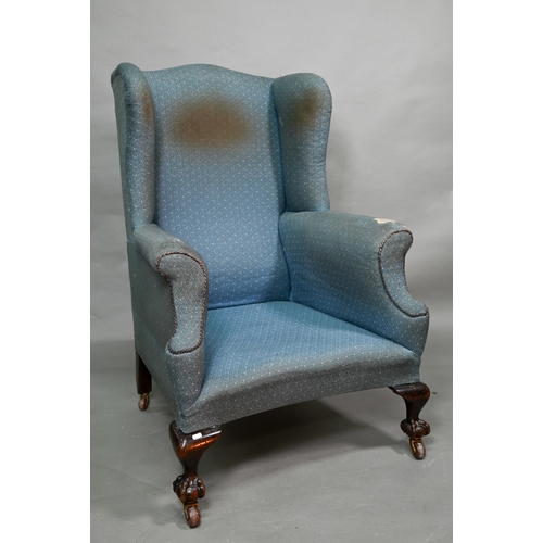 869 - A traditionally upholstered Queen Anne style wing armchair, with concave seat front, raised on short... 