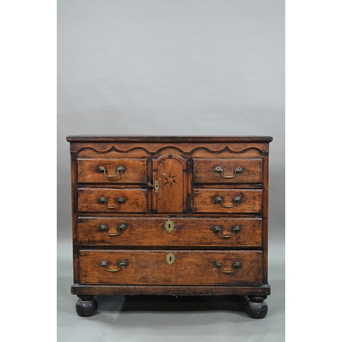 929 - An 18th century oak chest, the wavy frieze over a centre cupboard flanked by short two tier drawers,... 