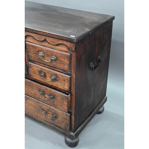 929 - An 18th century oak chest, the wavy frieze over a centre cupboard flanked by short two tier drawers,... 