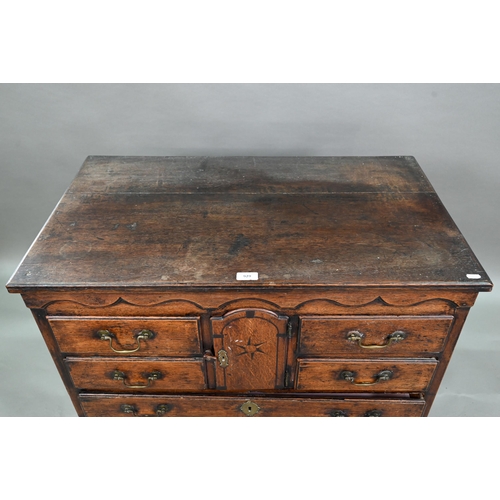 929 - An 18th century oak chest, the wavy frieze over a centre cupboard flanked by short two tier drawers,... 