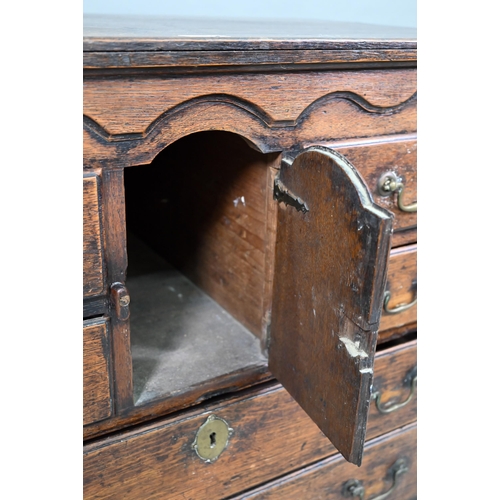 929 - An 18th century oak chest, the wavy frieze over a centre cupboard flanked by short two tier drawers,... 