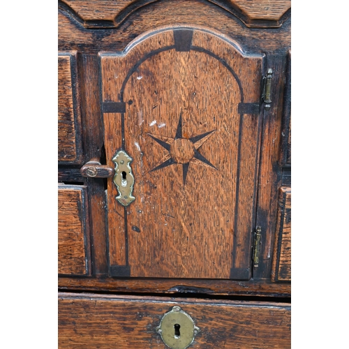 929 - An 18th century oak chest, the wavy frieze over a centre cupboard flanked by short two tier drawers,... 