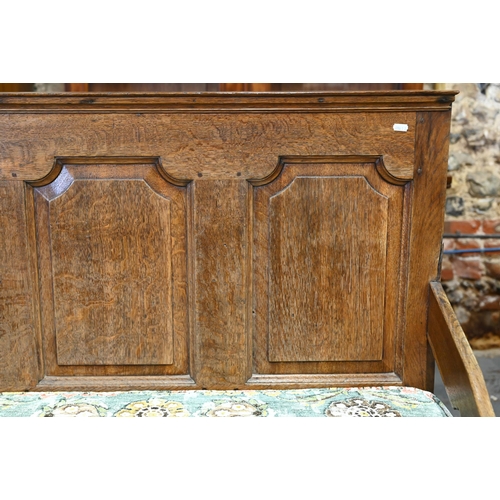 937 - A George III oak settle, the panelled back with shapes arms over a wood slat seat (and loose cushion... 