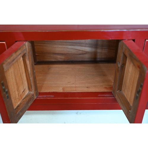 137 - A Chinese red lacquer sidetable with central cupboards and two drawers to each side, with brass fitt... 