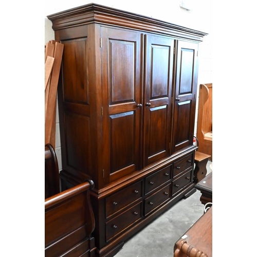 153 - A large modern stained hardwood triple wardrobe with panelled doors over six drawer base on low brac... 