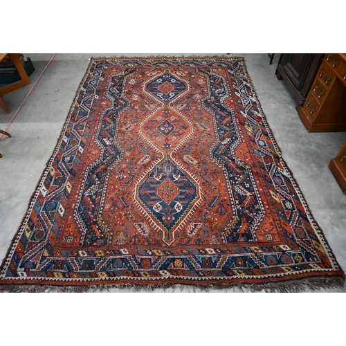 166 - A Persian Shiraz carpet with navy medallions on terracotta ground, 310 x 210 cm 