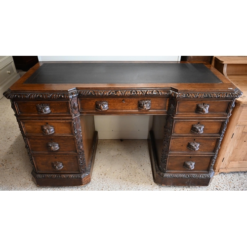 307 - A late Victorian Gothic Revival carved oak twin pedestal desk with nine drawers and 'Green Man' carv... 