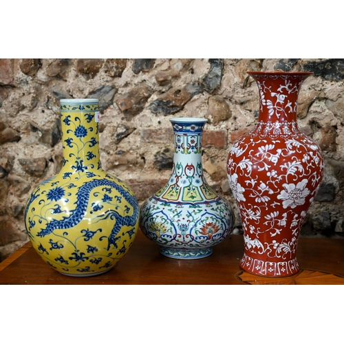 A Chinese doucai vase with Qianlong mark, 31 cm high to/w a blue and yellow 'dragon' vase with Xuande mark, 35 cm high and a coral ground baluster vase decorated in white enamels with floral designs, Kangxi mark, 42 cm high - All post Qing dynasty (3)
