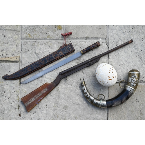 620 - An ornamental powder horn with metal mounts, a carved ostrich egg, a Tribal machete and an air rifle... 