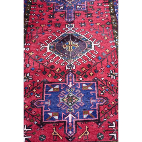 648 - A North West Persian runner, geometric medallions on red ground with navy borders 388 x 108cm