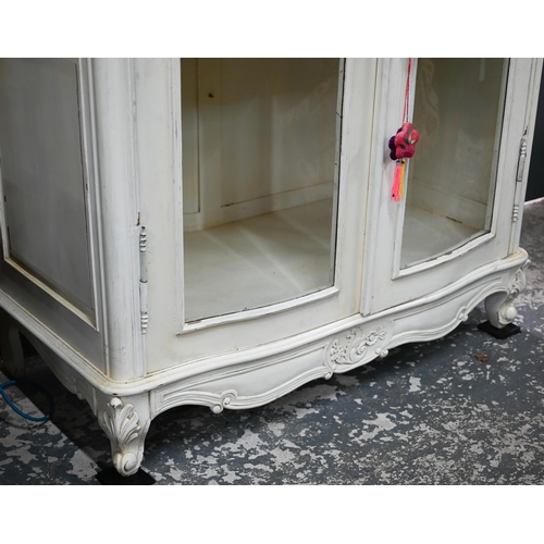 120 - A Continental painted part glazed-in cabinet, of serpentine form with ornate carved pediment, with t... 