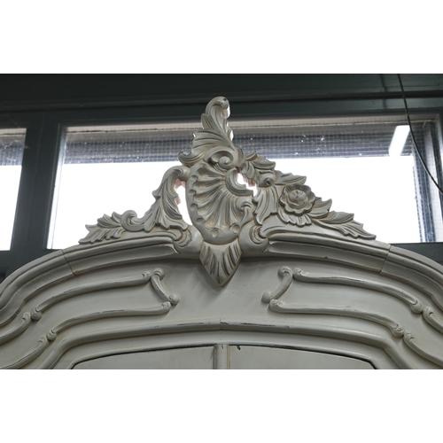 121 - A Continental painted part glazed-in cabinet, of serpentine form with ornate carved pediment, with t... 