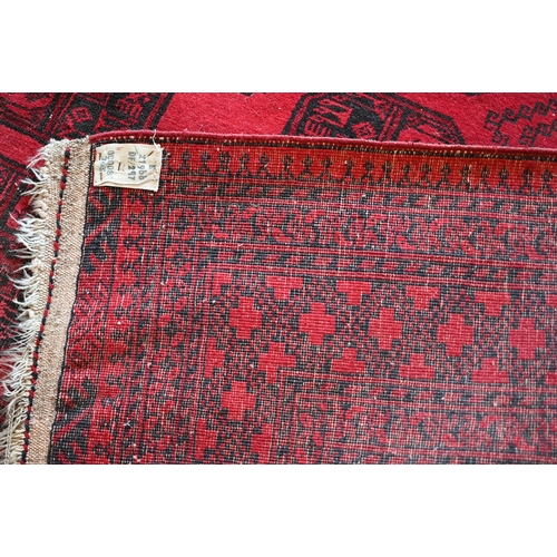 191 - An Afghan red ground carpet, repeating gul design and repeating borders