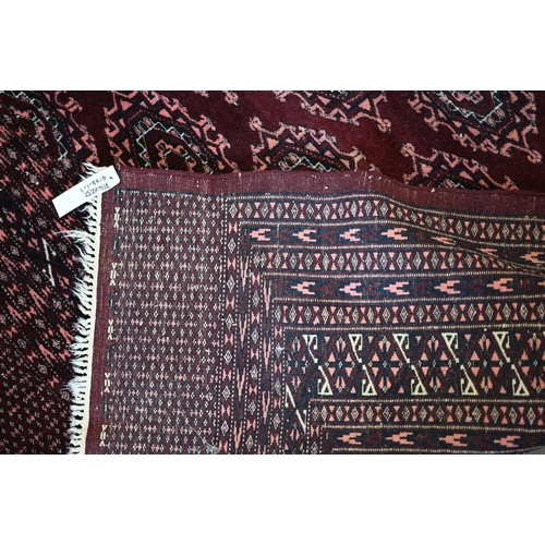 202 - A Pakistani Turkoman design wine ground carpet with repeating gul design within multi border, 312 x ... 