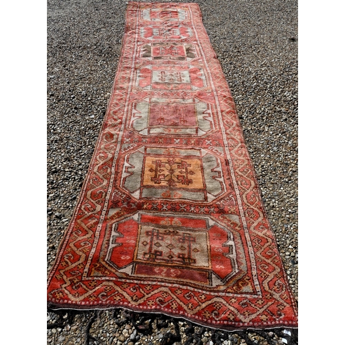 237 - A vintage Kurdish red ground runner with seven octagonal medallions, 440 x 93 cm (extreme woof/curve... 