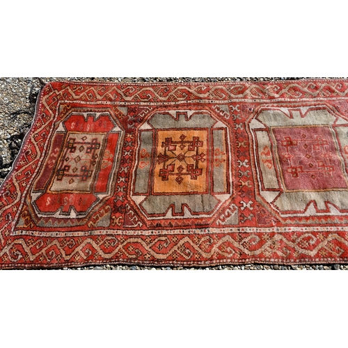 237 - A vintage Kurdish red ground runner with seven octagonal medallions, 440 x 93 cm (extreme woof/curve... 