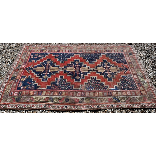 261 - A worn Caucasian kelleigh rug with geometric medallions on red/blue ground and repeating borders, 22... 