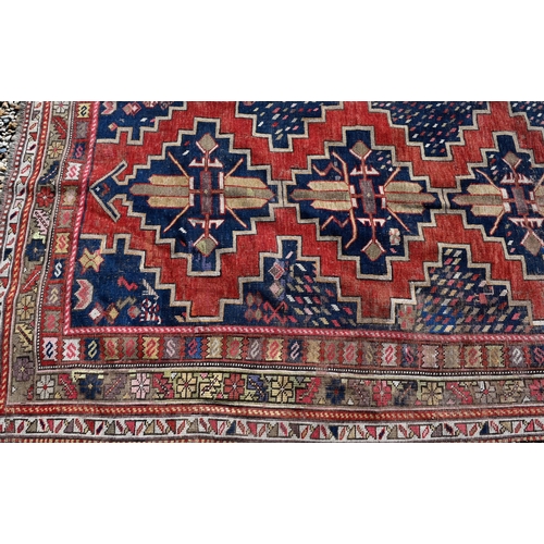 261 - A worn Caucasian kelleigh rug with geometric medallions on red/blue ground and repeating borders, 22... 