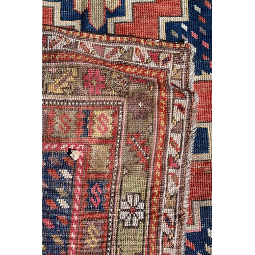 261 - A worn Caucasian kelleigh rug with geometric medallions on red/blue ground and repeating borders, 22... 