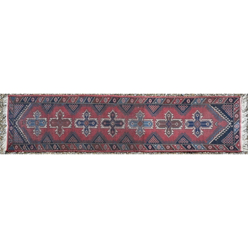 279 - A Caucasian geometric design red ground runner with seven lozenges to middle, 305 x 72 cm