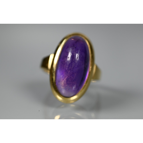 228 - A contemporary ring set with oval cabochon amethyst, yellow metal set stamped 750 Ka, size M, amethy... 