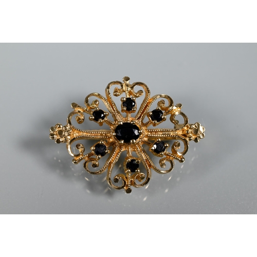 237 - An unmarked yellow metal scroll brooch set with seven small dark blue sapphires, approx 4.5g all in