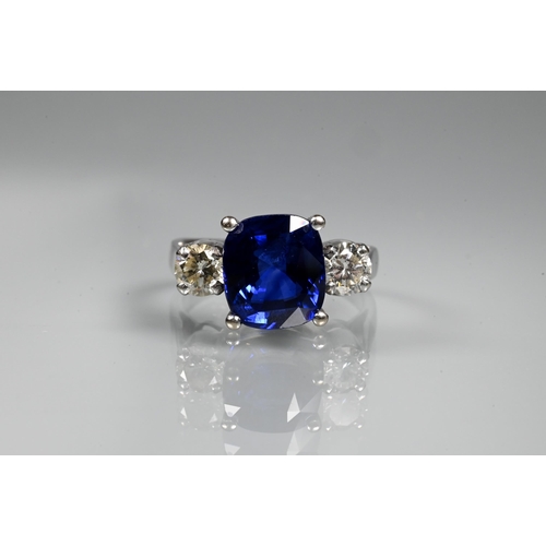 A modern sapphire and diamond three stone ring, the central blue cushion cut sapphire with two round brilliant cut diamonds to either side, claw set in (unmarked) 18ct white gold, size M