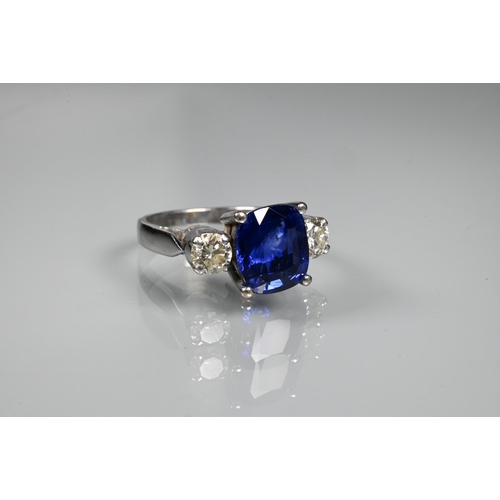 255 - A modern sapphire and diamond three stone ring, the central blue cushion cut sapphire with two round... 