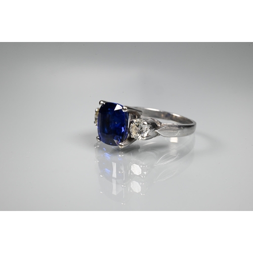 255 - A modern sapphire and diamond three stone ring, the central blue cushion cut sapphire with two round... 