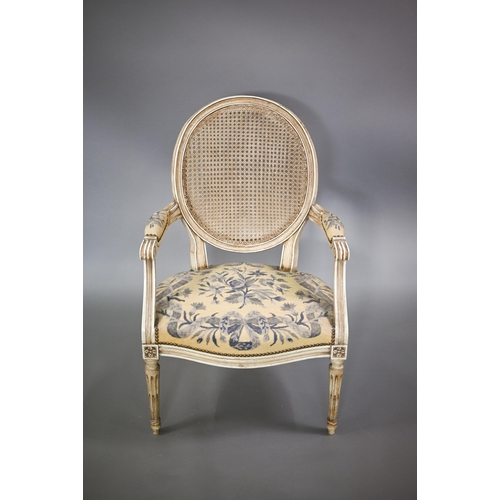 837 - A pair of French ivory painted cane panel backed salon elbow chairs, with floral needlepoint sprung ... 