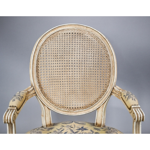 837 - A pair of French ivory painted cane panel backed salon elbow chairs, with floral needlepoint sprung ... 