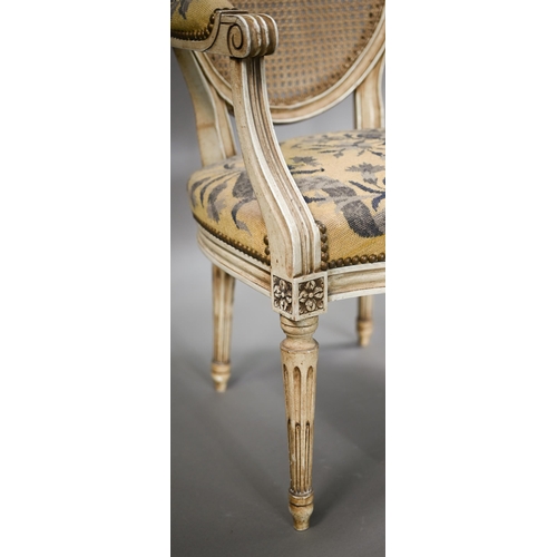 837 - A pair of French ivory painted cane panel backed salon elbow chairs, with floral needlepoint sprung ... 